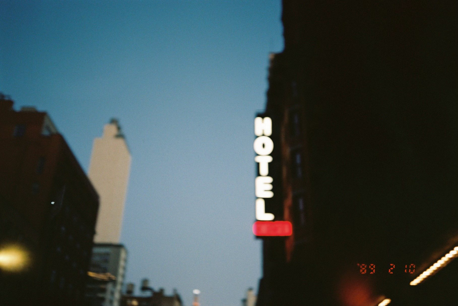 Blurry film photo of a vintage HOTEL neon sign at dusk